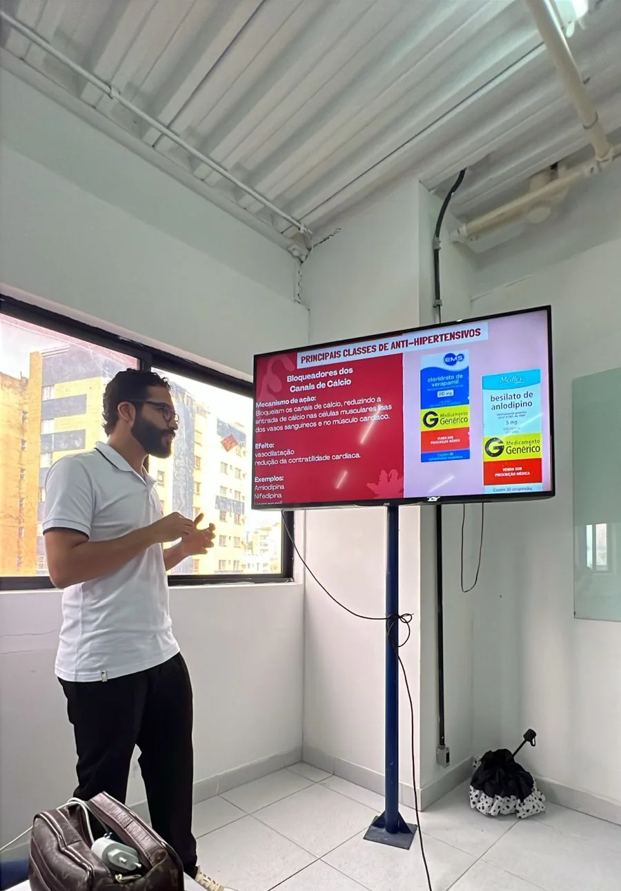 Daniel P Francisco apresentando um seminário em sala, com um slide projetado na tela ao lado
