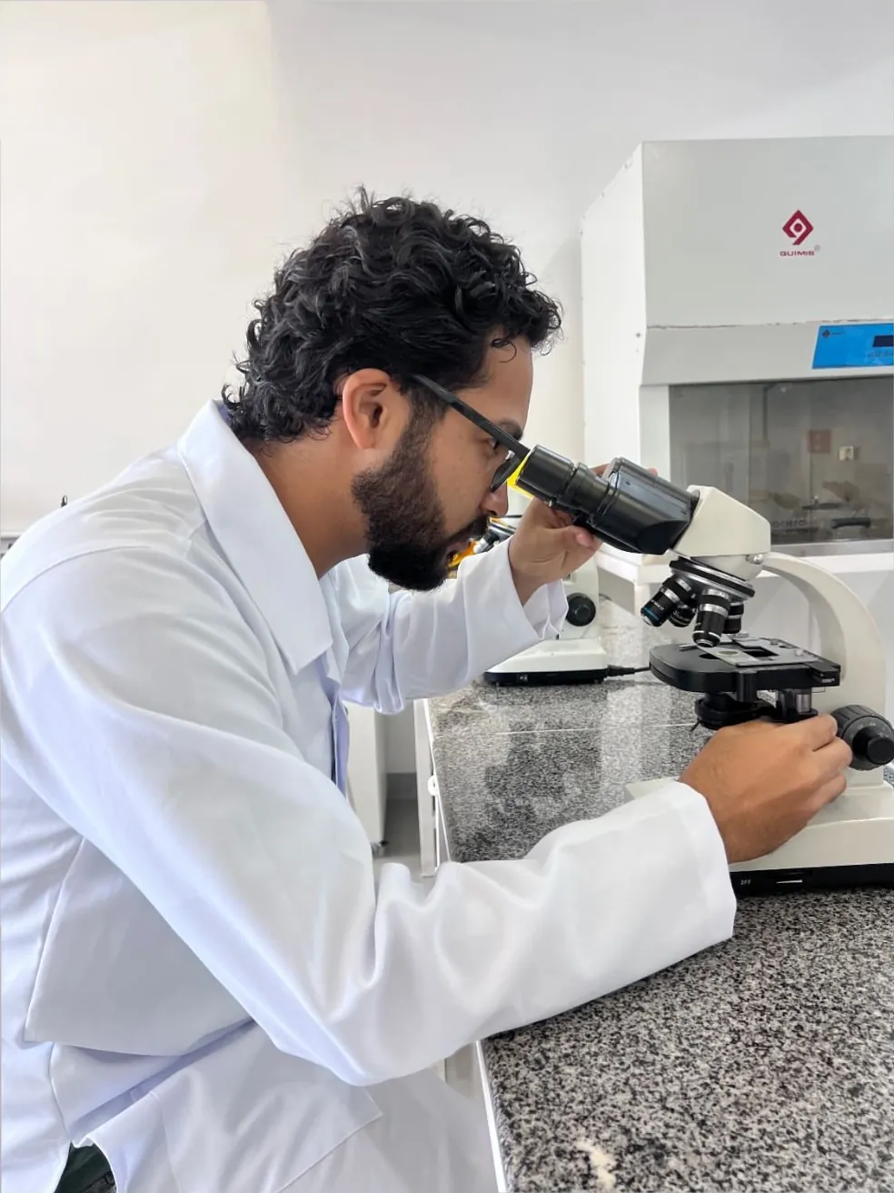 Daniel P Francisco de jaleco observando ao microscópio em um laboratório